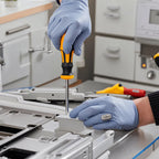 Gloved hands driving one of the screwdrivers into an appliance panel on a worktop.