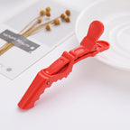 Red sectioning clip styled on a flat-lay with dried flowers, a printed card and a white plate, angled close view.