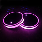 Two LED cup holder coasters lit magenta-purple, glossy black tops, dark perforated surface.