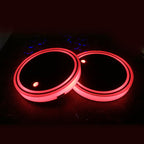 Two LED cup holder coasters glowing red, plain black tops, on the dark perforated tray surface.