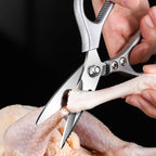 Close-up of the shears cutting through a raw chicken leg and bone against a black background.