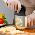 Hands pressing the wavy crinkle cutter through a potato on a wooden board, cut lattice chips scattered around.