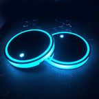 Pair of LED cup holder coasters lit in cyan, glossy black tops, on a dark perforated mat.