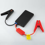 Jump starter pack connected to its booster cable, red and black clamps spread open on a grey backdrop